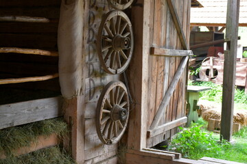 A close up on several wooden wheels on rims attached to wooden wall and situated next to wooden door to a barn, house, or hut seen on a sunny summer day on a Polish countryside