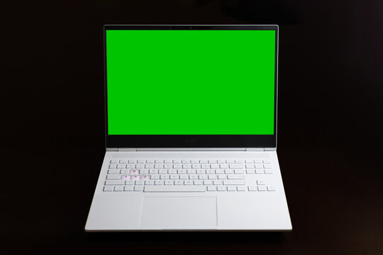 An isolated image on the black background of a white simple slim and gaming laptop with green chroma key screen for using as mockup and template.