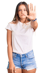 Beautiful caucasian woman wearing casual white tshirt doing stop sing with palm of the hand. warning expression with negative and serious gesture on the face.