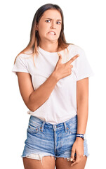Beautiful caucasian woman wearing casual white tshirt pointing aside worried and nervous with...