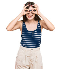 Young beautiful caucasian girl wearing casual clothes and glasses doing ok gesture like binoculars sticking tongue out, eyes looking through fingers. crazy expression.