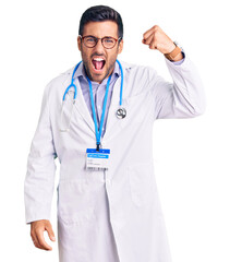 Young hispanic man wearing doctor uniform and stethoscope angry and mad raising fist frustrated and furious while shouting with anger. rage and aggressive concept.