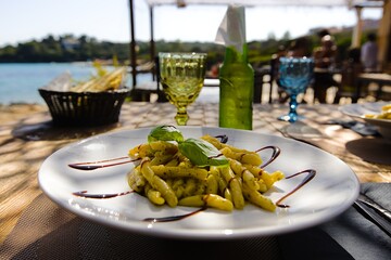 A plate of penne pasta on Sardinia, adorned with pesto, drizzled with balsamic vinegar, and garnished with fresh basil leaves. - obrazy, fototapety, plakaty