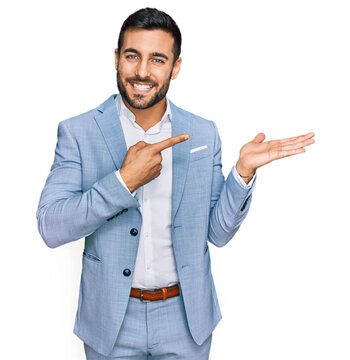 Young hispanic man wearing business jacket amazed and smiling to the camera while presenting with hand and pointing with finger.