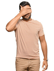 Handsome hispanic man wearing casual clothes covering eyes with hand, looking serious and sad. sightless, hiding and rejection concept