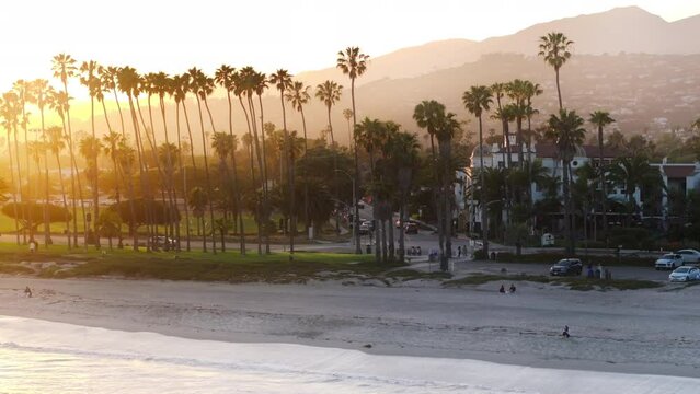 Drone flying over Pacific Ocean waves washing Santa Barbara beach, California, USA. City landmark in the sunset light. Panoramic landscape of streets and luxury houses of resort city, 4k footage 