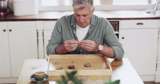 Senior man, marijuana and joint roll to smoke in preparation for medical THC, CBD or drug in kitchen at home. Mature male person licking paper, rolling or preparing natural herb plant or cannabis
