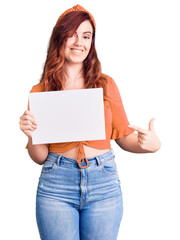 Fototapeta premium Young beautiful woman holding cardboard banner with blank space smiling happy pointing with hand and finger
