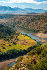 A wide river winds through a valley in Lesotho with fields of crops on the banks and mountains in...