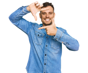 Young hispanic man wearing casual denim jacket smiling making frame with hands and fingers with happy face. creativity and photography concept.