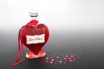 Love potion heart shaped bottle for Valentines Day with red heart confetti decorations on gradient gray. Lovers relationship romantic abstract concept.
