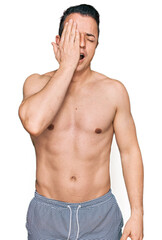 Handsome young man wearing swimwear shirtless yawning tired covering half face, eye and mouth with hand. face hurts in pain.