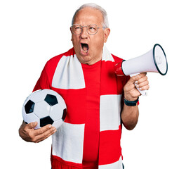 Senior man with grey hair football hooligan holding ball and using megaphone angry and mad...