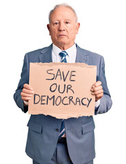 Senior handsome grey-haired man holding save our democracy cardboard banner thinking attitude and sober expression looking self confident