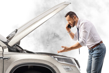 Stressed young man with a car looking under the hood and talking on the phone