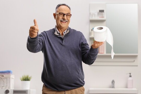 Smiling mature man holding a toilet paper roll and gesturing thumbs up