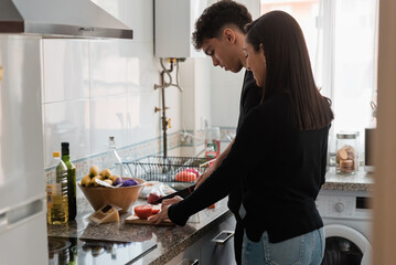 Happy ethnic couple cutting veggies while cooking together in kitchen
