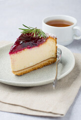 Piece of cheesecake with berry sauce on a plate and a cup of tea, close up