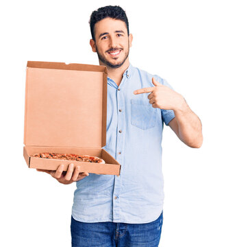 Young hispanic man holding delivery pizza box pointing finger to one self smiling happy and proud