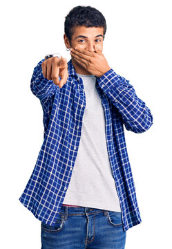 Young african amercian man wearing casual clothes laughing at you, pointing finger to the camera with hand over mouth, shame expression