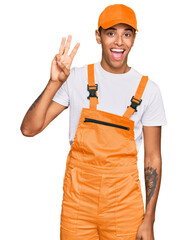 Young handsome african american man wearing handyman uniform showing and pointing up with fingers number three while smiling confident and happy.