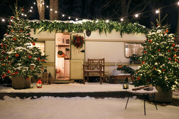 Mobile home Caravan with terrace at night, Mobile home decorated with Christmas decor. Festive atmosphere - lights, blankets, Christmas trees. Caravan camping. mobile home trailer. Selective focus
