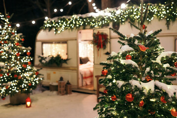 Mobile home Caravan with terrace at night, Mobile home decorated with Christmas decor. Festive atmosphere - lights, blankets, Christmas trees. Caravan camping. mobile home trailer. Selective focus