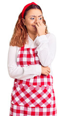 Young latin woman wearing apron looking stressed and nervous with hands on mouth biting nails. anxiety problem.