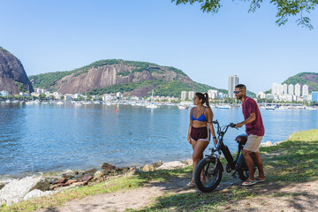 Young couple walking along the shore, talking, pushing a bicycle.