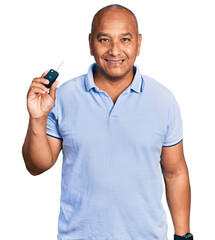 Hispanic middle age man holding key of new car looking positive and happy standing and smiling with...
