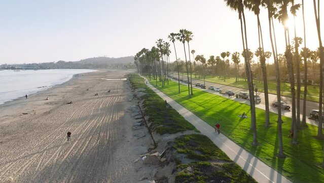 Aerial view of Santa Barbara coastline in sunset light, California, USA. Overhead shot of people enjoying vacation on the sandy beach. Sun rays breaking through the palm trees along road, 4k footage 