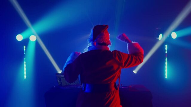 DJ Santa Claus mixing tracks in a nightclub at a Christmas and New Year party or Corporate events. Senior disc jockey as Santa listening music, headphones, laptop, mixer controller player, turntable.