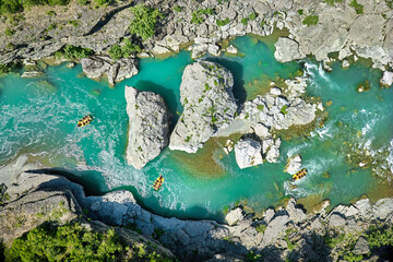 White water rafting.  Adventure and sport. A yellow raft floating among the rocks on the crystal clear, blue-green water. Perpendicular drone view of the rafters floating on Vjose river, Albania.