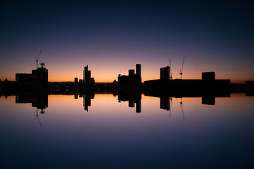 Reflection of Manchester Skyline at Sunrise with Skyscraper Silhouettes on the Golden Horizon and Blue Morning Sky