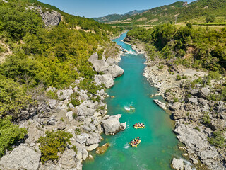 White water rafting.  Adventure and sport. A yellow raft floating among the rocks on the crystal clear, blue-green water. Perpendicular drone view of the rafters floating on Vjose river, Albania. - obrazy, fototapety, plakaty