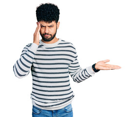 Fototapeta premium Young arab man with beard wearing casual striped sweater confused and annoyed with open palm showing copy space and pointing finger to forehead. think about it.