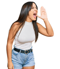 Young beautiful hispanic girl wearing casual clothes shouting and screaming loud to side with hand on mouth. communication concept.