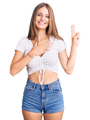 Young beautiful blonde woman wearing casual white tshirt smiling swearing with hand on chest and...