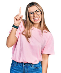 Hispanic young woman wearing casual t shirt and glasses pointing finger up with successful idea. exited and happy. number one.