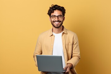 A happy IT specialist in casual wear, holding a laptop and smiling, solving digital mysteries, isolated on a solid background. - obrazy, fototapety, plakaty