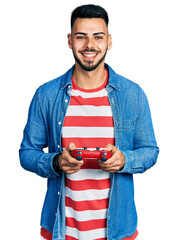 Young hispanic man with beard playing video game holding controller smiling with a happy and cool...