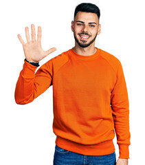 Fototapeta premium Young hispanic man with beard wearing casual orange sweater showing and pointing up with fingers number five while smiling confident and happy.