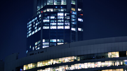 The glass facades of a modern skyscrapers at night. Modern glass office in city. Big glowing windows in modern offices buildings at night. In rows of windows light shines.