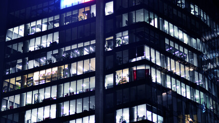 Fototapeta na wymiar Fragment of the glass facade of a modern corporate building at night. Modern glass office in city. Big glowing windows in modern office buildings at night, in rows of windows light shines. 