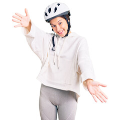 Beautiful brunette young woman wearing bike helmet and sporty clothes looking at the camera smiling with open arms for hug. cheerful expression embracing happiness.