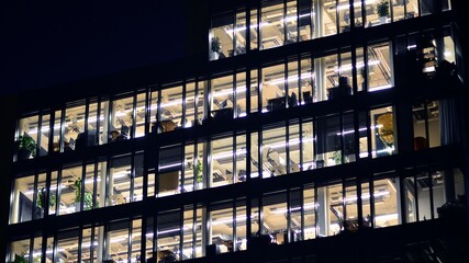 Fragment of the glass facade of a modern corporate building at night. Modern glass office  in city. Big glowing windows in modern office buildings at night, in rows of windows light shines.  - Powered by Adobe