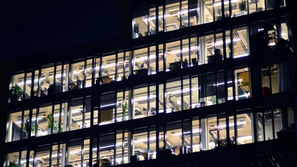 Fotobehang Fragment of the glass facade of a modern corporate building at night. Modern glass office  in city. Big glowing windows in modern office buildings at night, in rows of windows light shines.  © Grand Warszawski