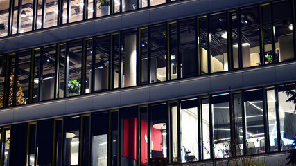 Fragment of the glass facade of a modern corporate building at night. Modern glass office  in city. Big glowing windows in modern office buildings at night, in rows of windows light shines. 