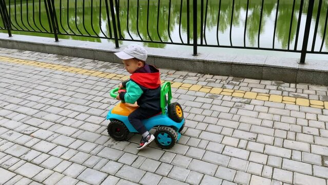 Lovely little kid riding his toy car pushing from the floor. Child rides along the artificial pond.