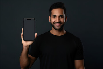 Dark-haired man in a black T-shirt holding a smartphone in front of him with a blank screen on dark gray background